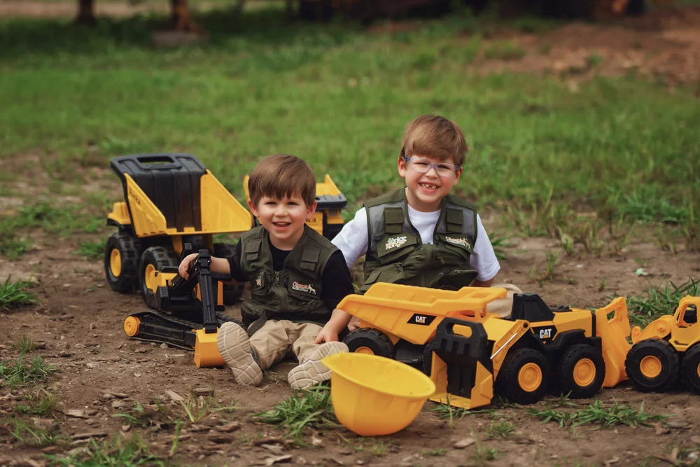 Two siblings smiling among their toy construction trucks