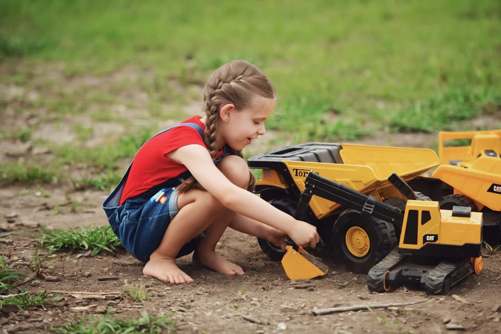 Child crouching to load a large yellow toy truck