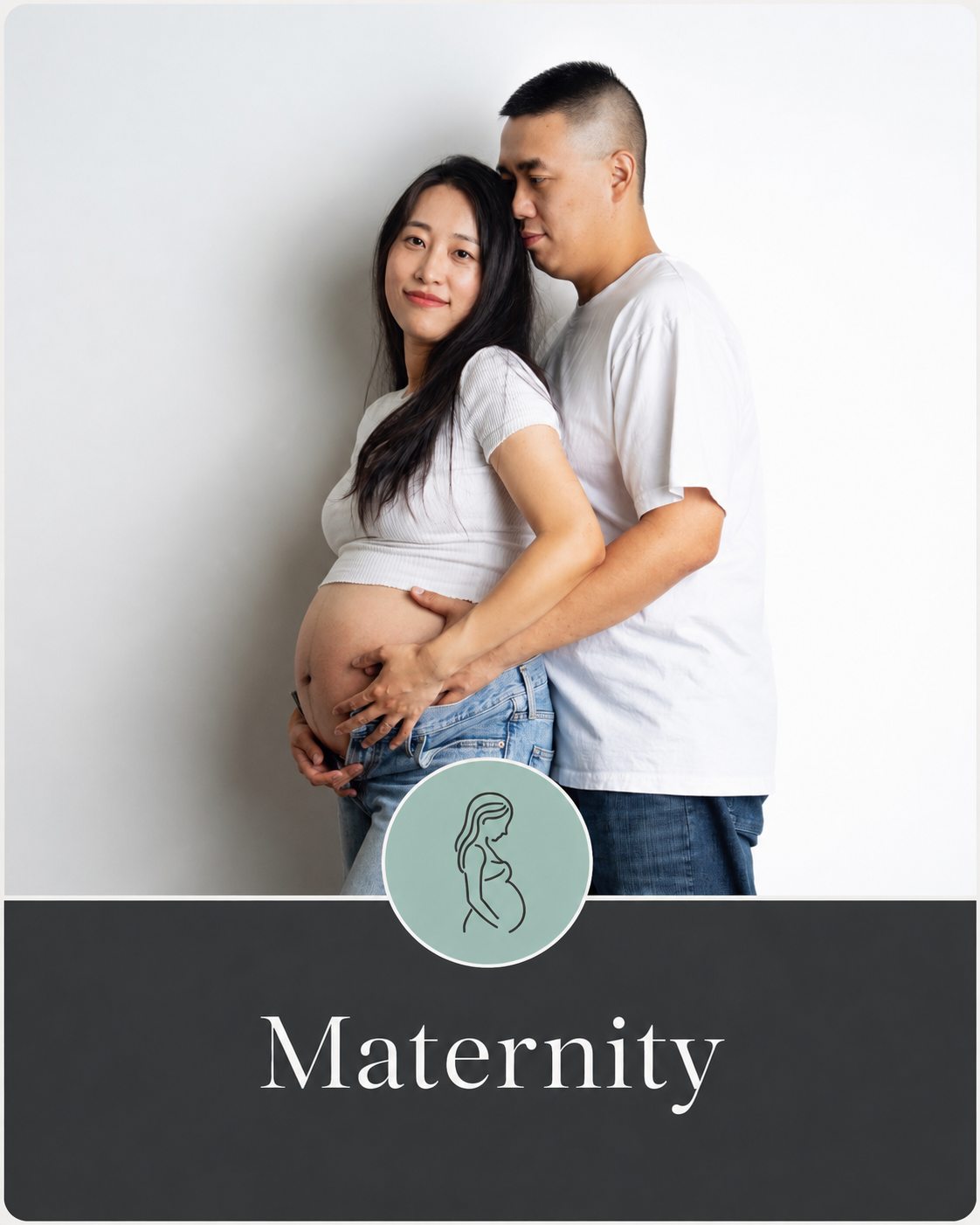 Maternity photo of a pregnant woman with a man standing behind her, both in casual white shirts, against a plain white background. The woman is smiling and touching her belly, while the man is gently holding her belly with both hands. There is a circular icon of a pregnant woman and the word "Maternity" below.