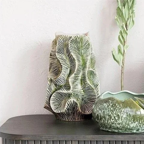 This stoneware organic vase, crafted from high-temperature fired ceramic, features a textured design and a narrow opening, creating a rustic and refined effect. The vase's green color adds a fresh and elegant touch. It can be used as a decorative acc