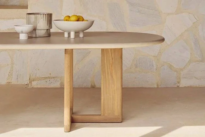 Blending modern sophistication with natural beauty, the outdoor dining table features a sleek, oblong-shaped concrete top set on a solid reclaimed teak base; both materials known for their strength and resilience against the elements. The wood grain 