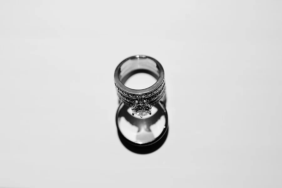 Close-up of a diamond engagement ring on a reflective surface, showing the ring's design and its reflection.