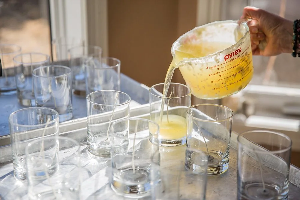 Person pouring melted wax from a Pyrex measuring cup into glass candle holders.