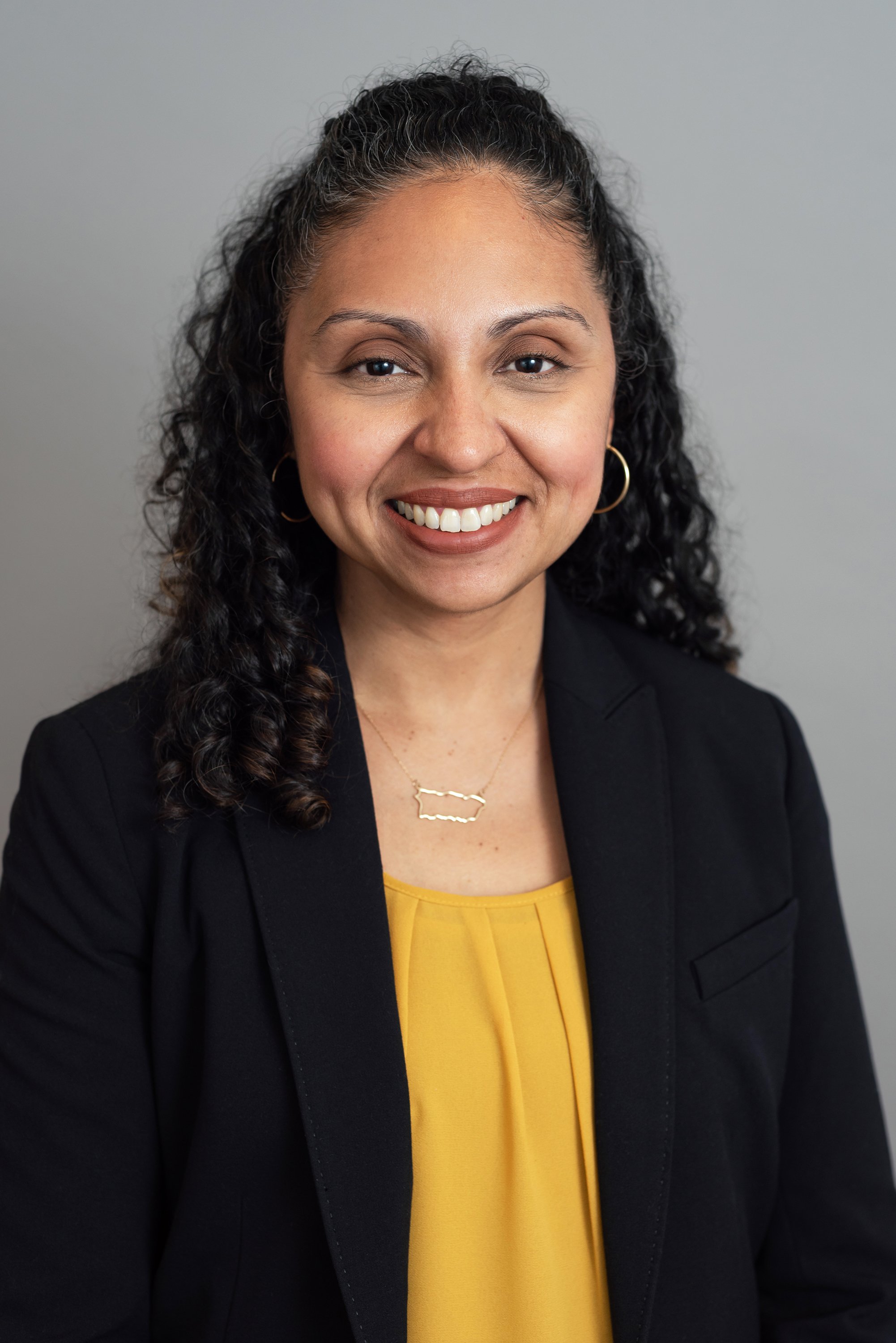  Corporate headshot of a woman in a gold colored top and black jacket by Ari Scott, NYC headshot photographer. 