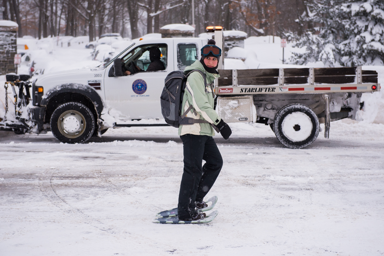 7:51am – Ashley Lazarz, a dietician at Maine Medical Center, snowshoes to work along Deering Ave. In the background, Dave Blackwell plows the entrance to Deering Oaks Park.