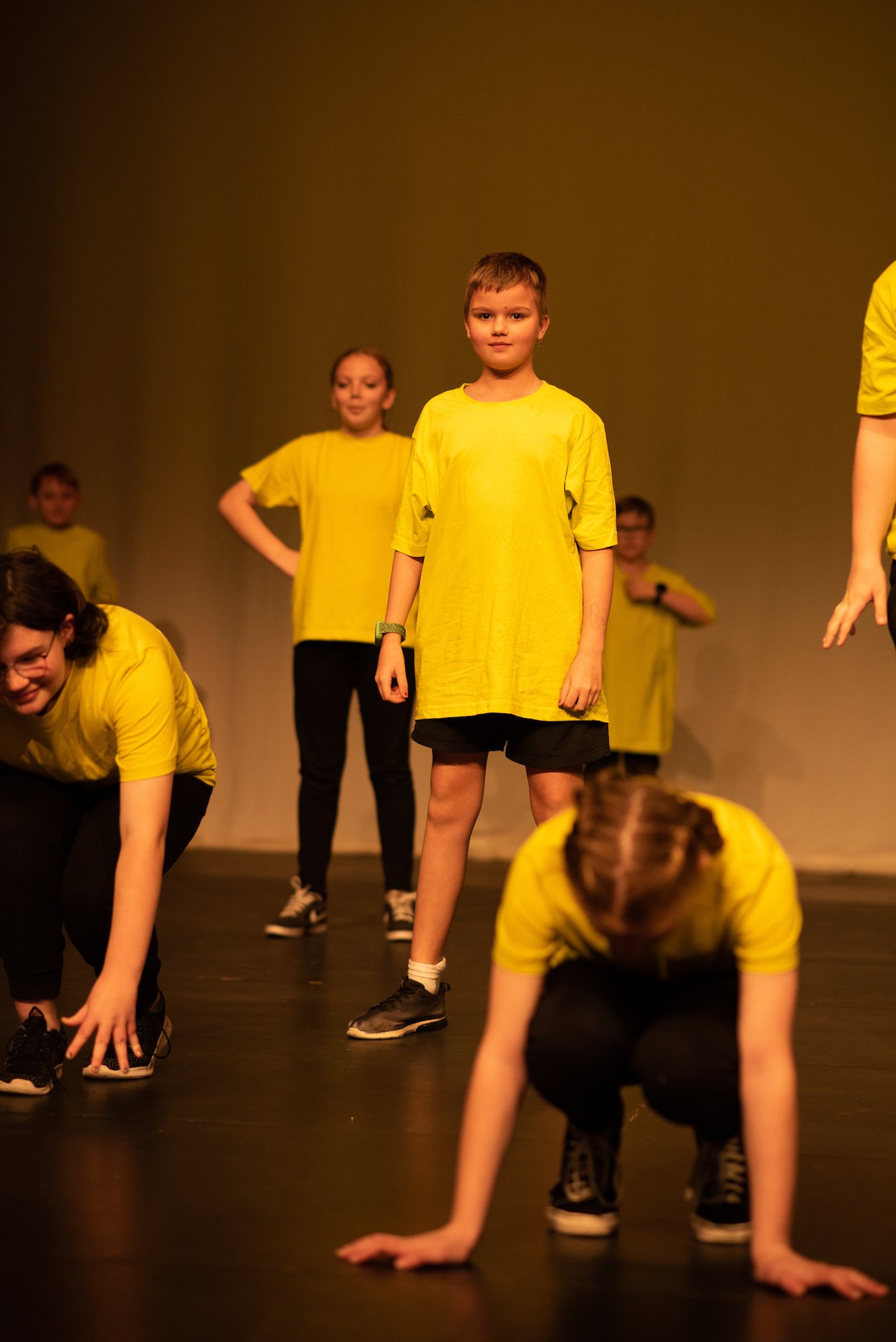  students wearing yellow two crouching in foreground and ensemble standing in background  