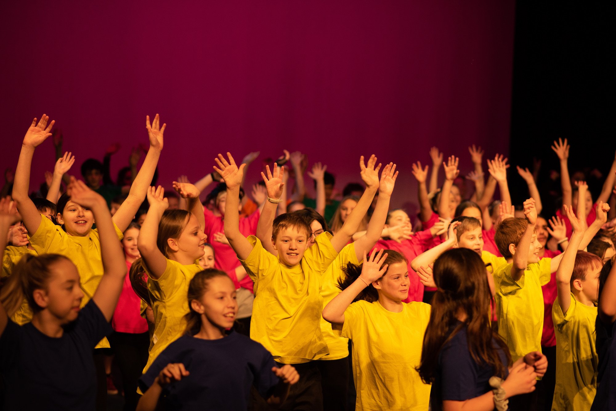  dozens of students dancing on stage joyfully arms raised  