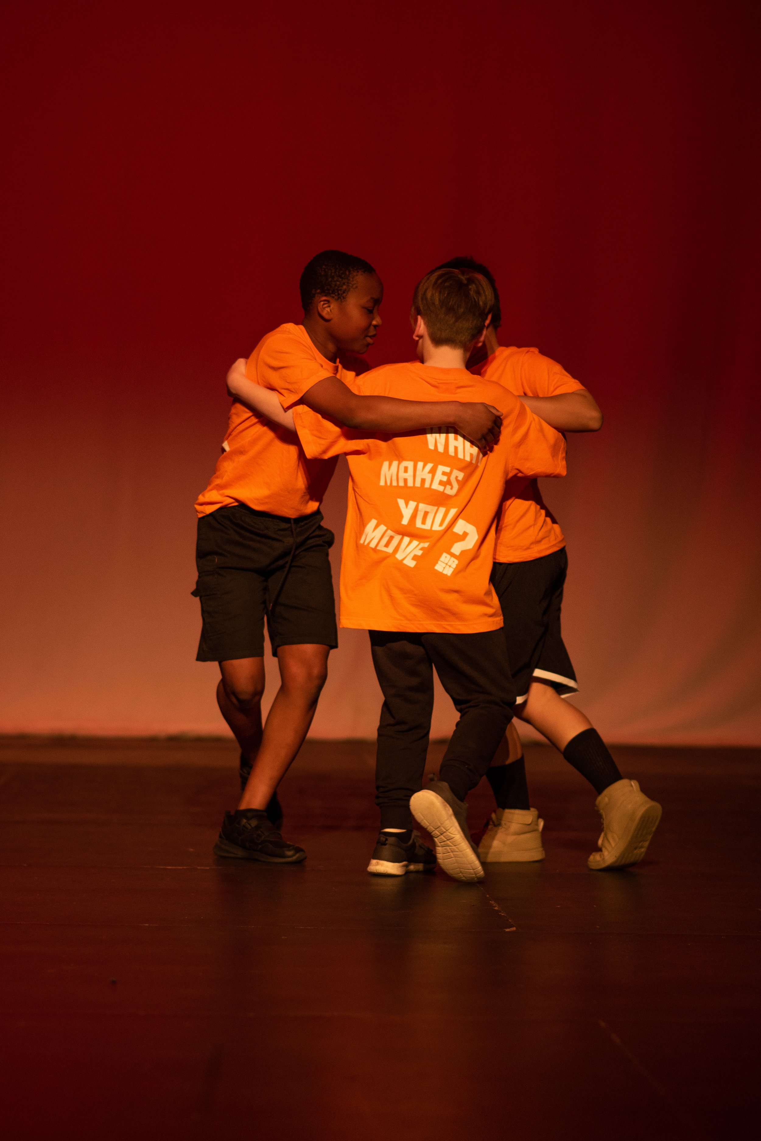3 boys huddled together dancing onstage 