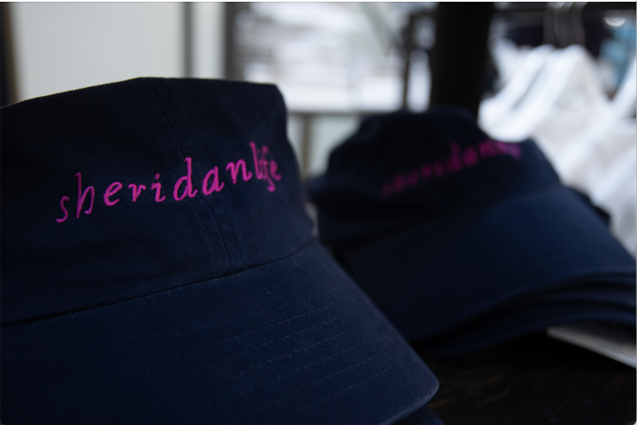  A collection of navy hats with magenta  Sheridan Life over the brim of the hat.  