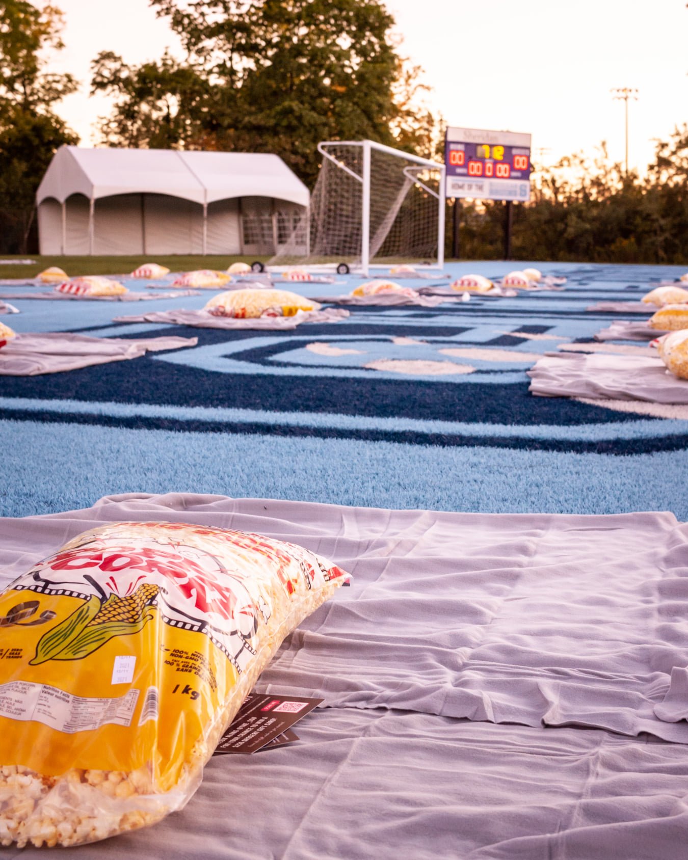  A close-up look at a large popcorn bag on a mat, on the left side. In the distance, more popcorn bags on the mat at the outdoor field at Sheridan College. 