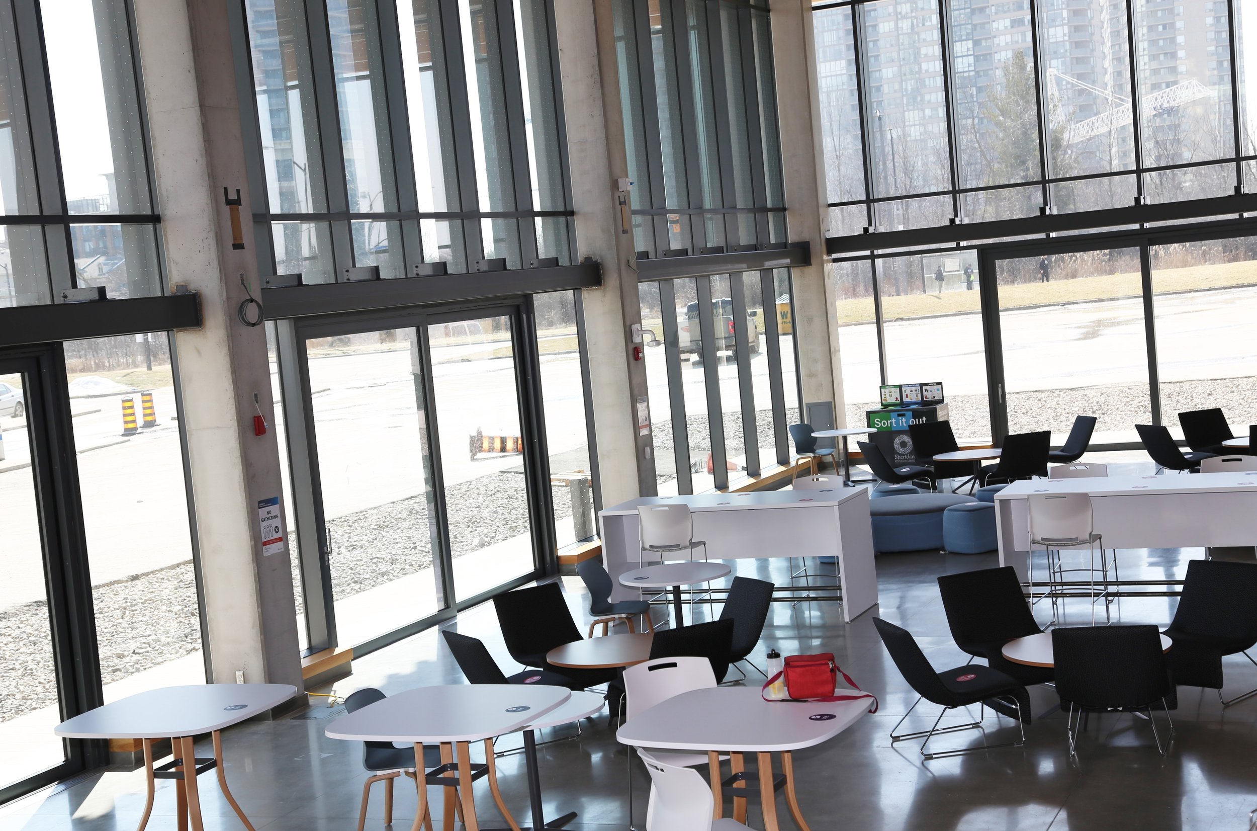  A side view of inside the Sheridan College Mississauga campus Student Centre atrium with desks, chairs and high ceiling glass windows.  