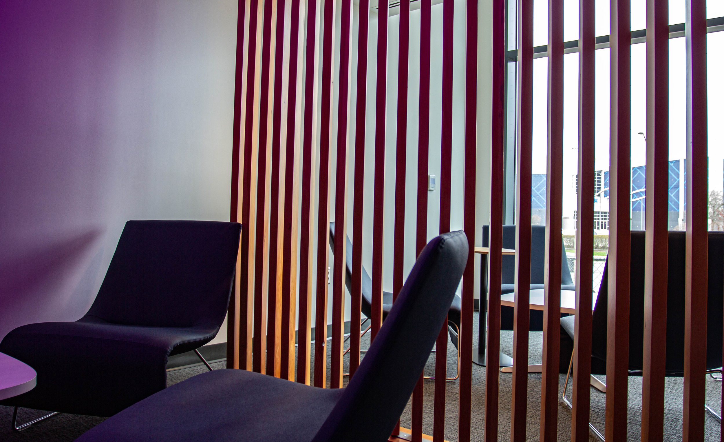  The 2nd floor Quiet Room in the HMC Student Centre. A panel of wooden vertical bars shows a little behind the wall. Two reclined seats in the room, with two more seats on the opposite side of the wall.   