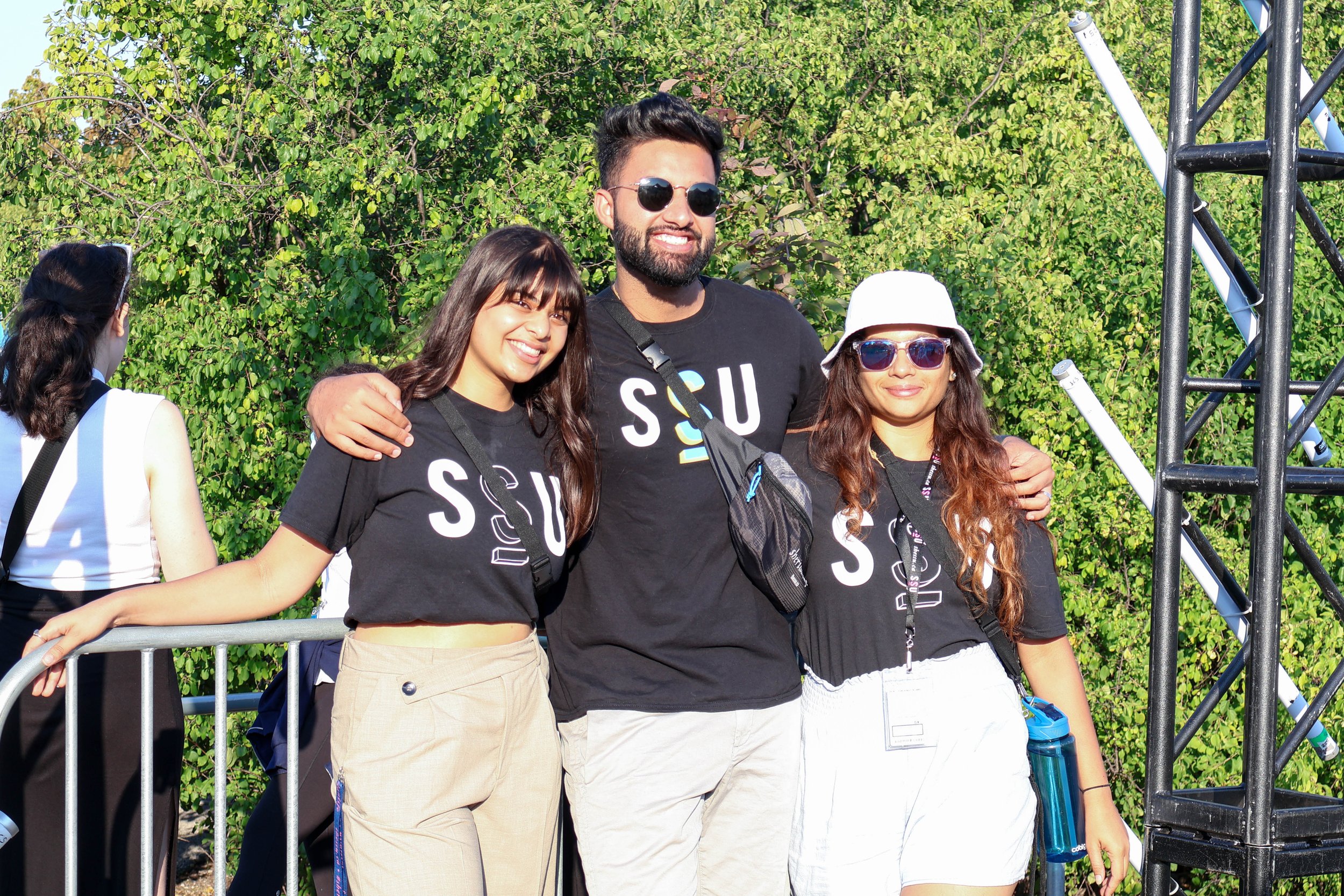  Three students standing outside an event gate, smiling in black t-shirts with the SSU logo on the front.  