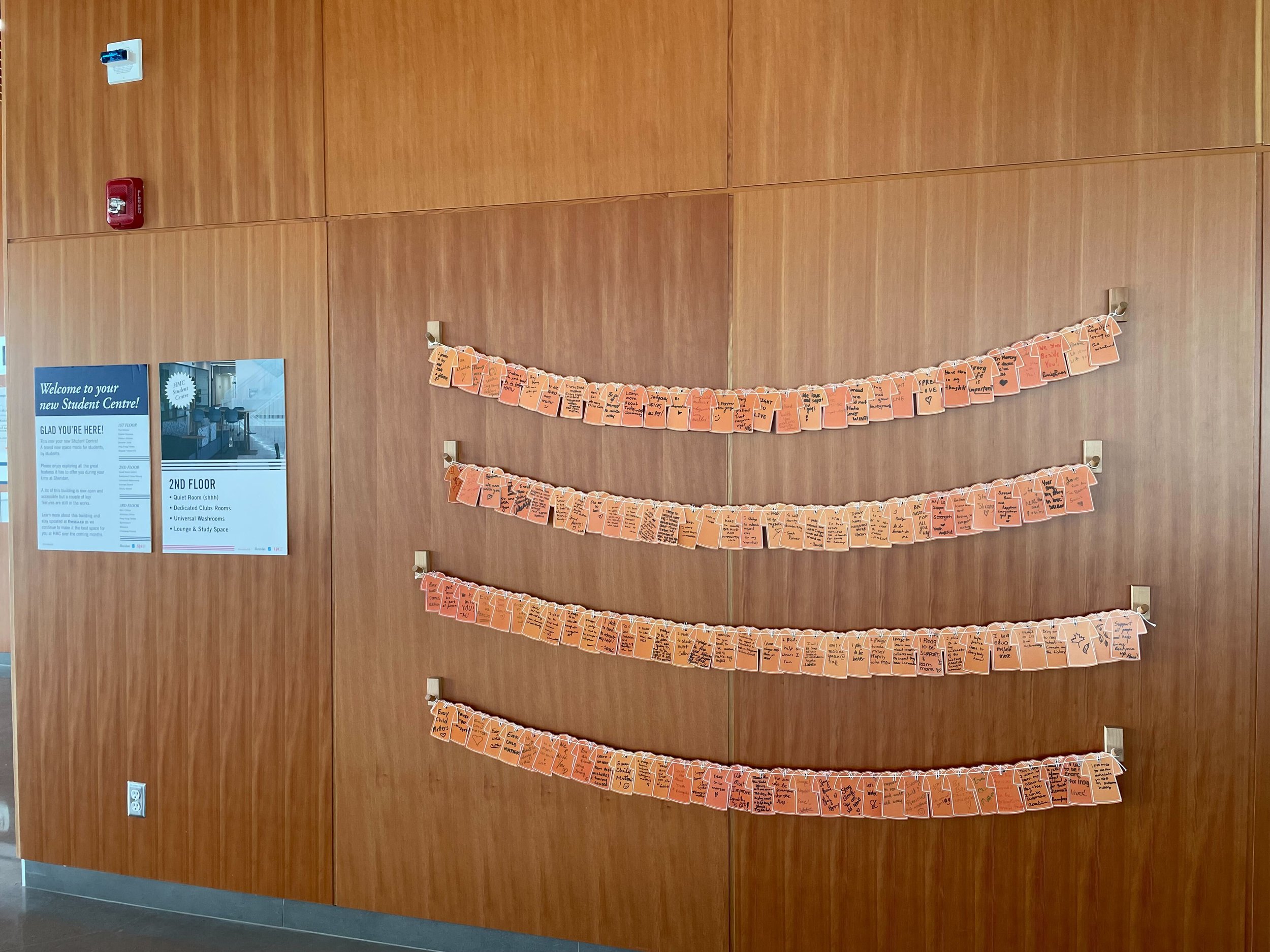  A wall at the HMC Student Centre with paper orange shirts posted on the wall with encouraging and hopeful message. 