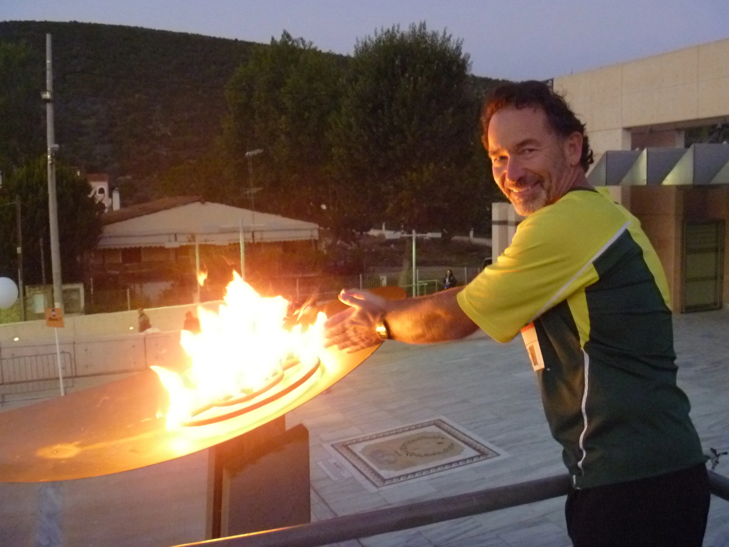Bruce warming his hands at the Olympic flame in the town of marathon, Greece, before running the Athens marathon.