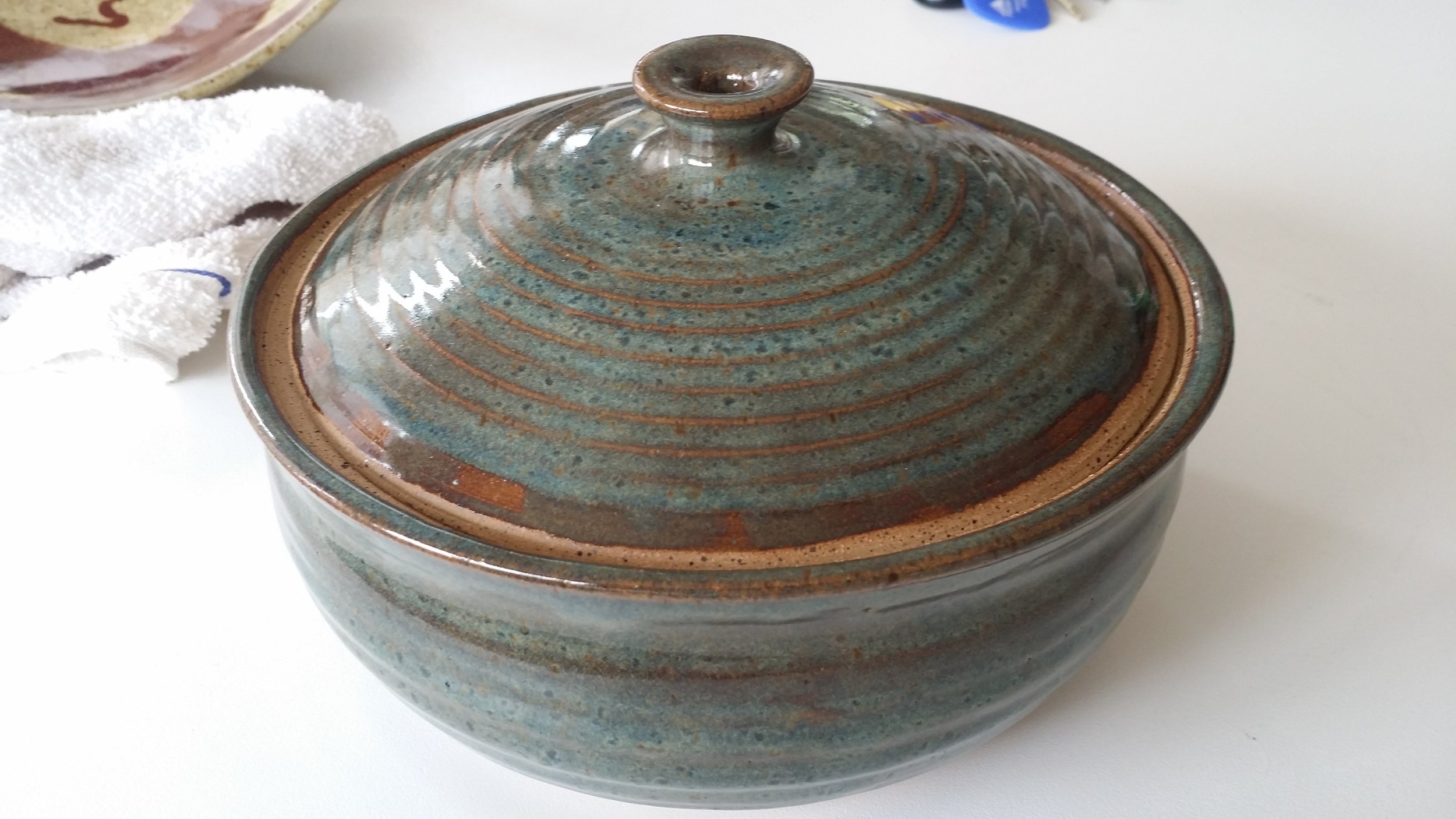 This is another multi-process piece. The casserole is thrown on the pottery wheel and the top is thrown on the wheel with a plaster bowl shape mold using calipers to ensure its the right size to fit the casserole base. You form a handle while making the top piece.