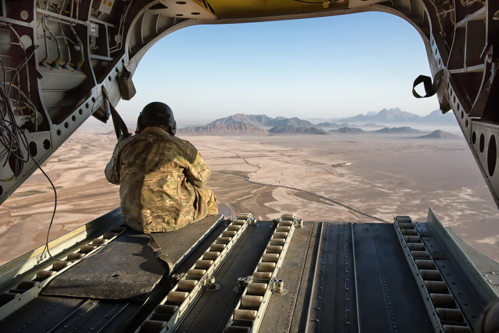 A US Army Soldier and aircrewman sits on the ramp of a chinook helicopter while flying at 1,500 feet (Lash-e Juwayn, Afghanistan).