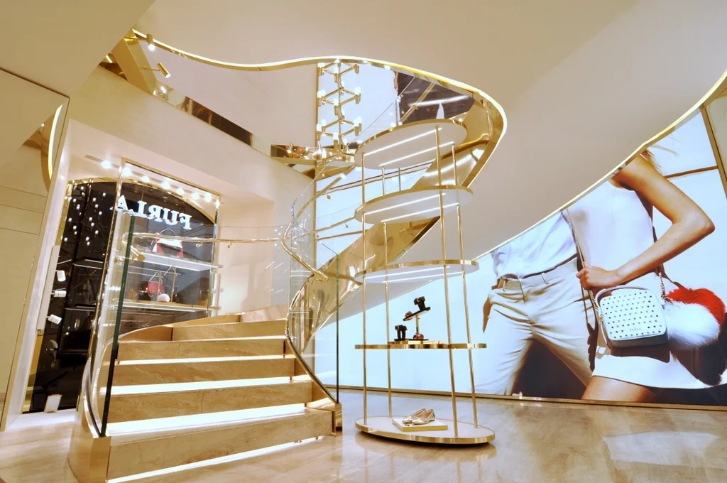   Scala ellittica per Furla Roma: &nbsp;scala in acciaio e vetro a forma ellittica, finitura in oro lucido. Parapetti in vetro extrachiaro curvo, corrimano in acciaio lucido e dorato. 