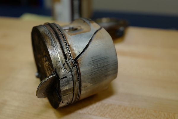 Volkswagen piston damage from timing belt failure. Required total engine replacement. Round coin shaped object embedded into top of piston is an intake valve that snapped off when piston hit it when camshaft went out of time with rotating crankshaft when timing belt broke.