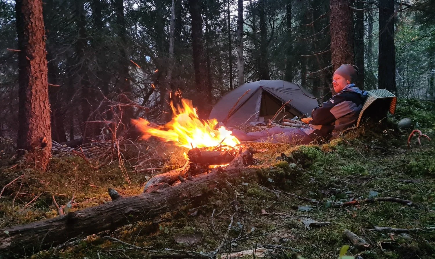 Mann sitter ved bål og koser seg.