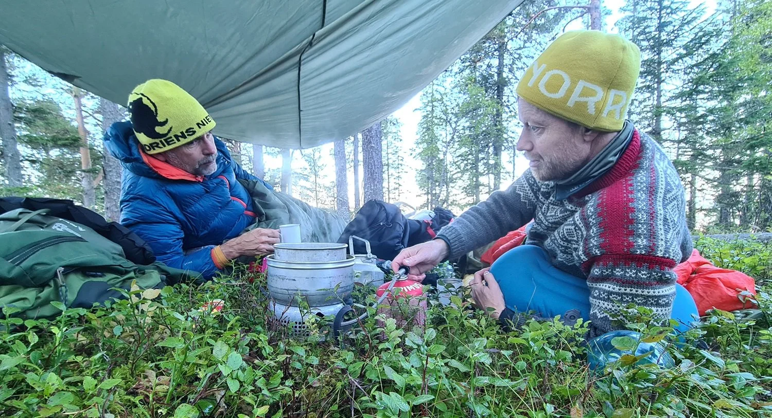 To menn drikker kaffe under en tarp.