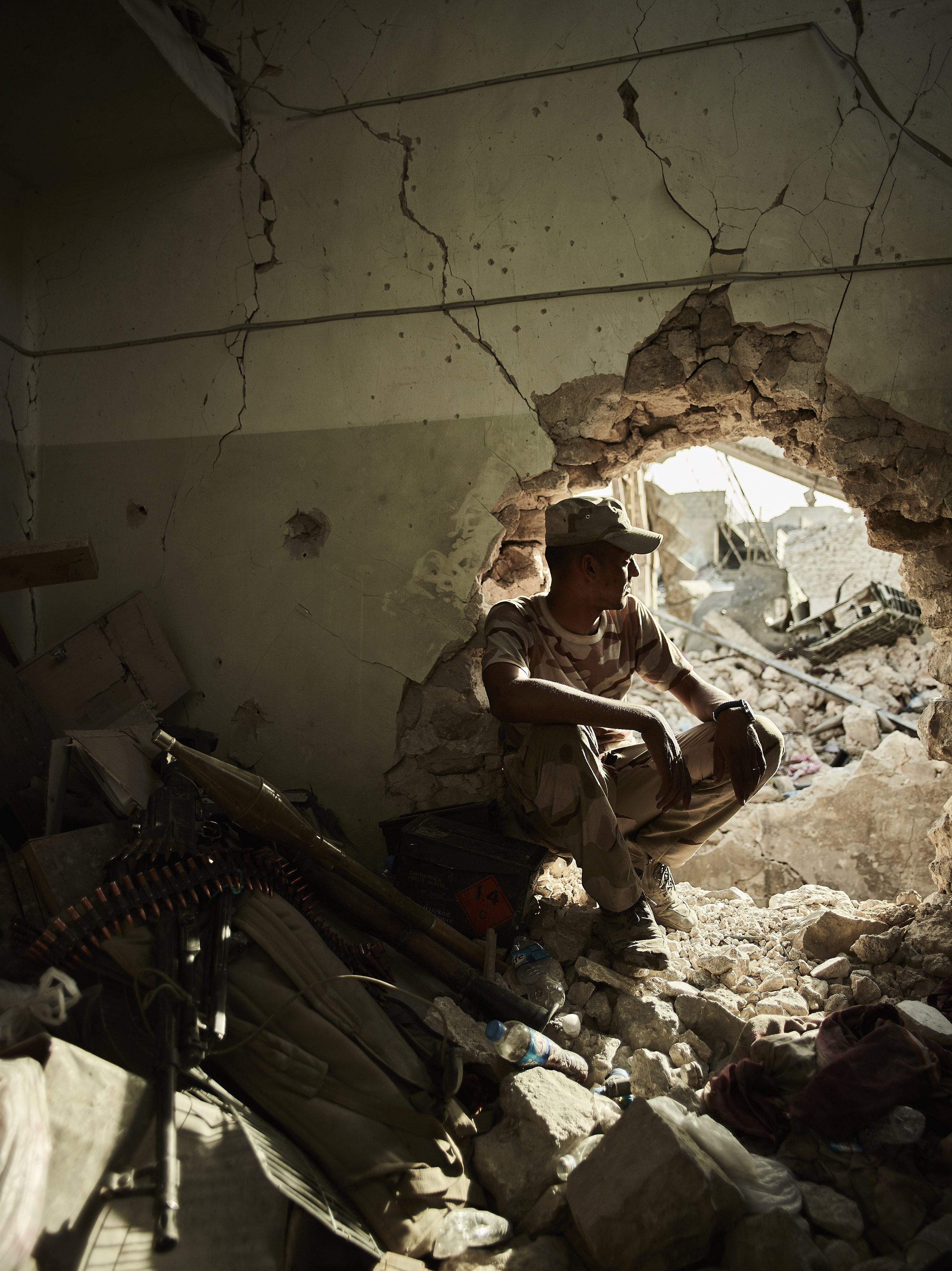 An Iraqi soldier peers through a hole in a building, West Mosul