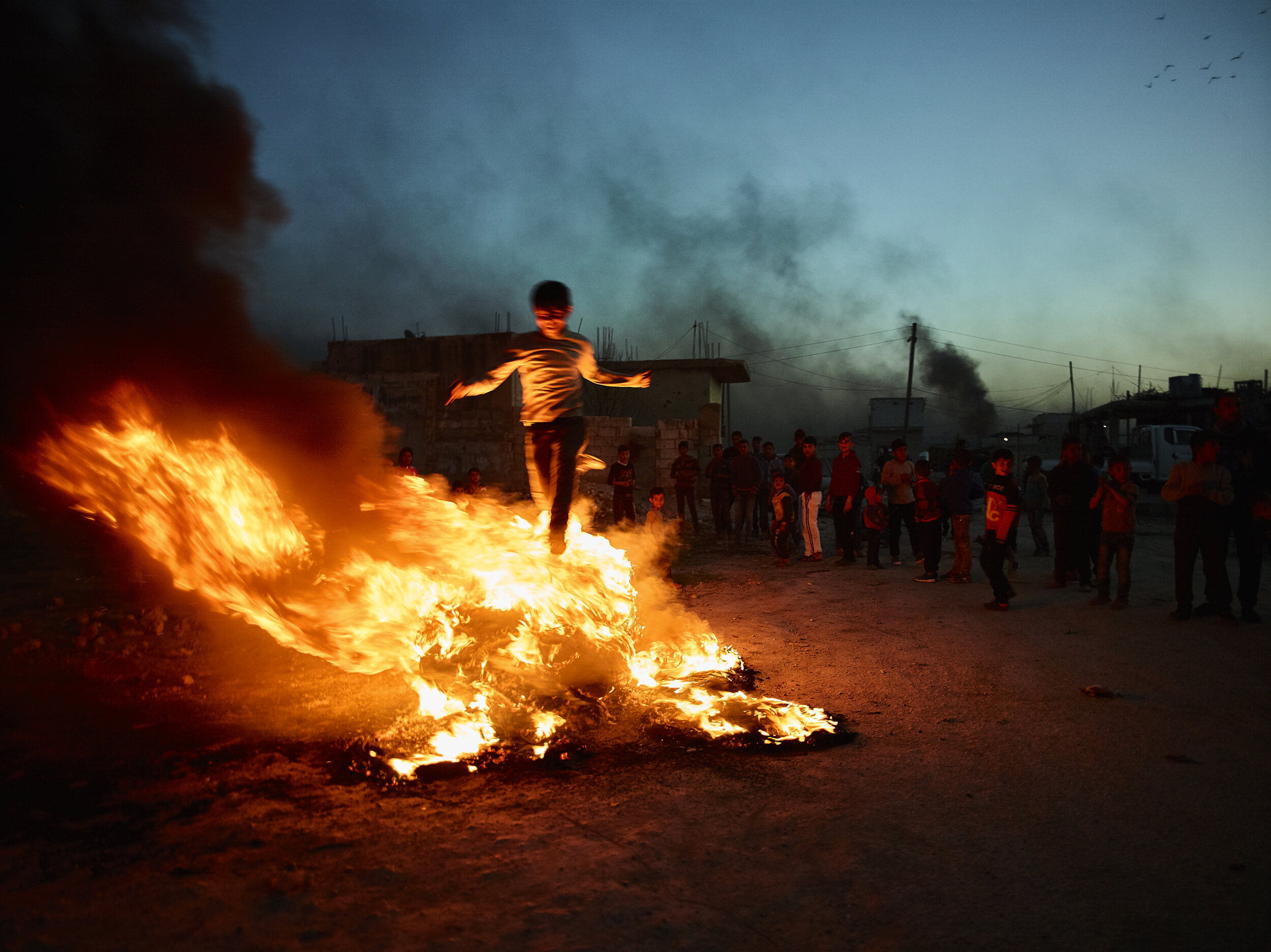 A young boy jumps over flaming tires during Newroz celebrations in Kobane