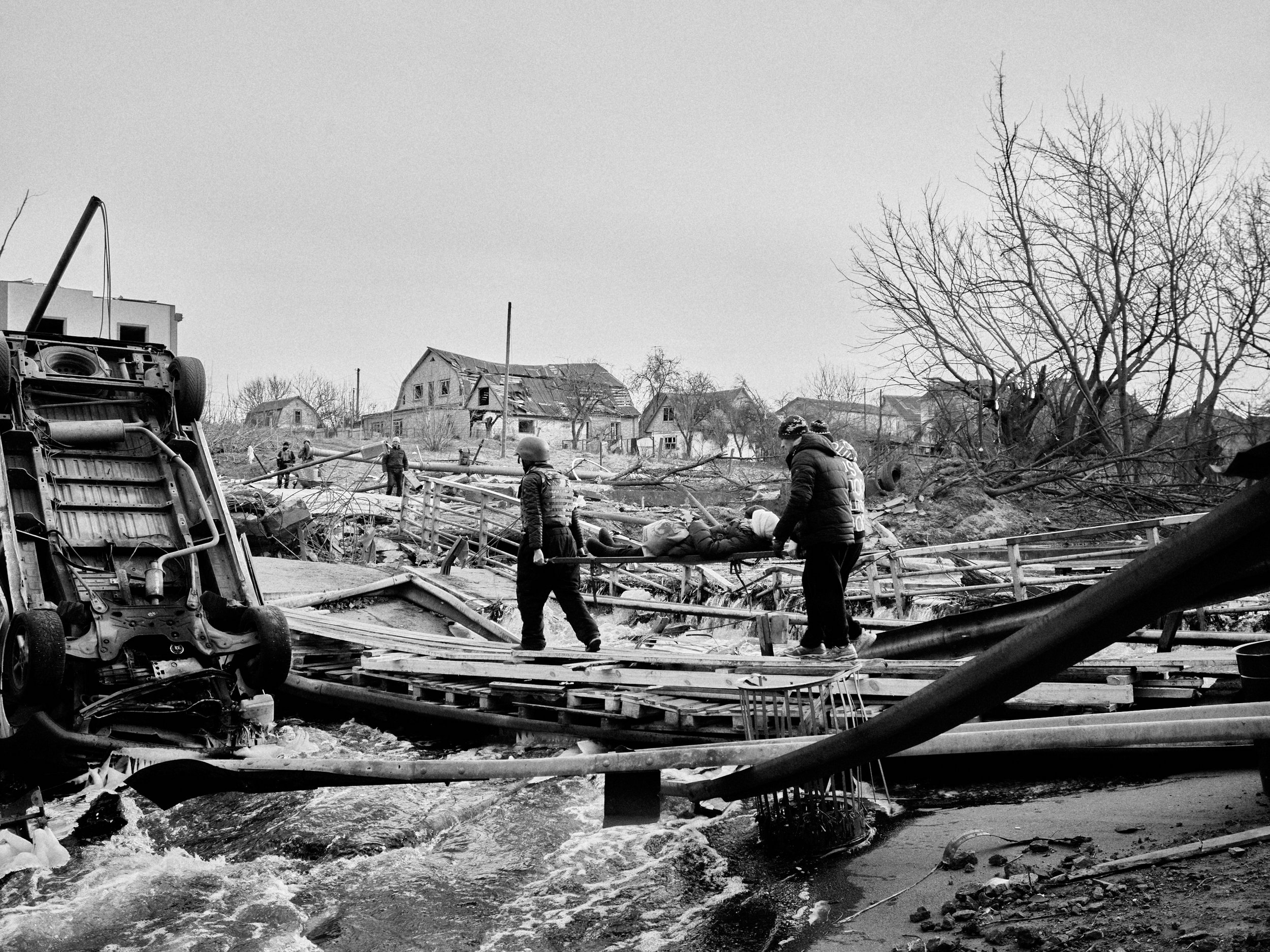 A woman is carried across a destroyed bridge in Irpin, Kyiv Oblast