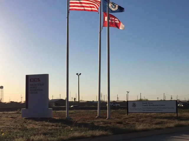 Outside the detention center in Dilley, TX—with the Corrections Corporation of America flag next to the US flag
