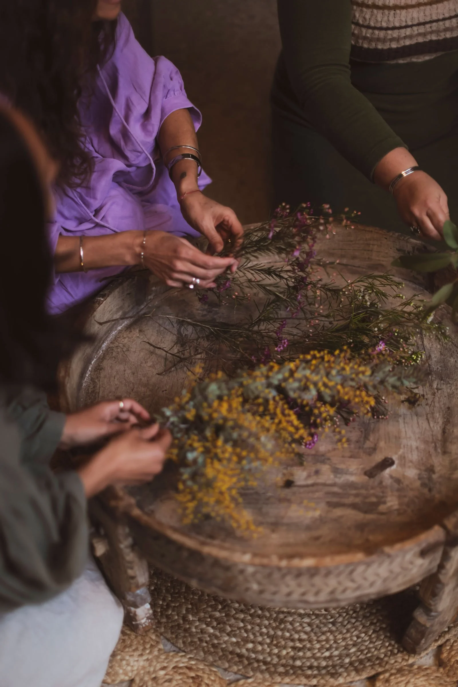 People arranging flower bouquets with yellow and purple flowers on a rustic wooden table.