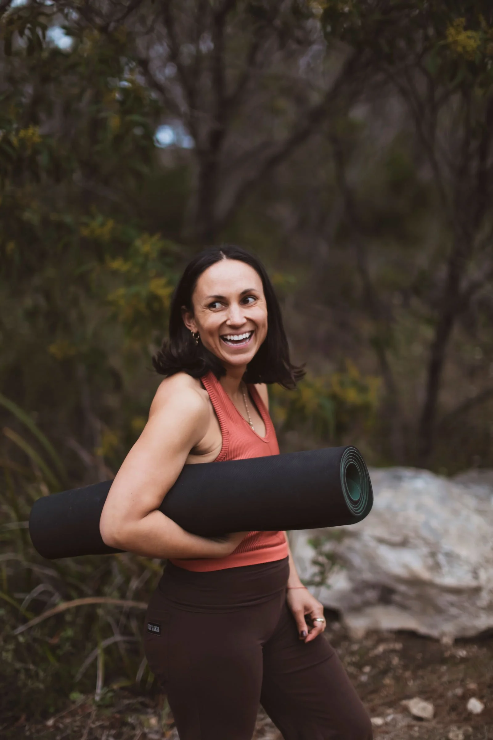 Woman outdoors holding a rolled yoga mat and smiling