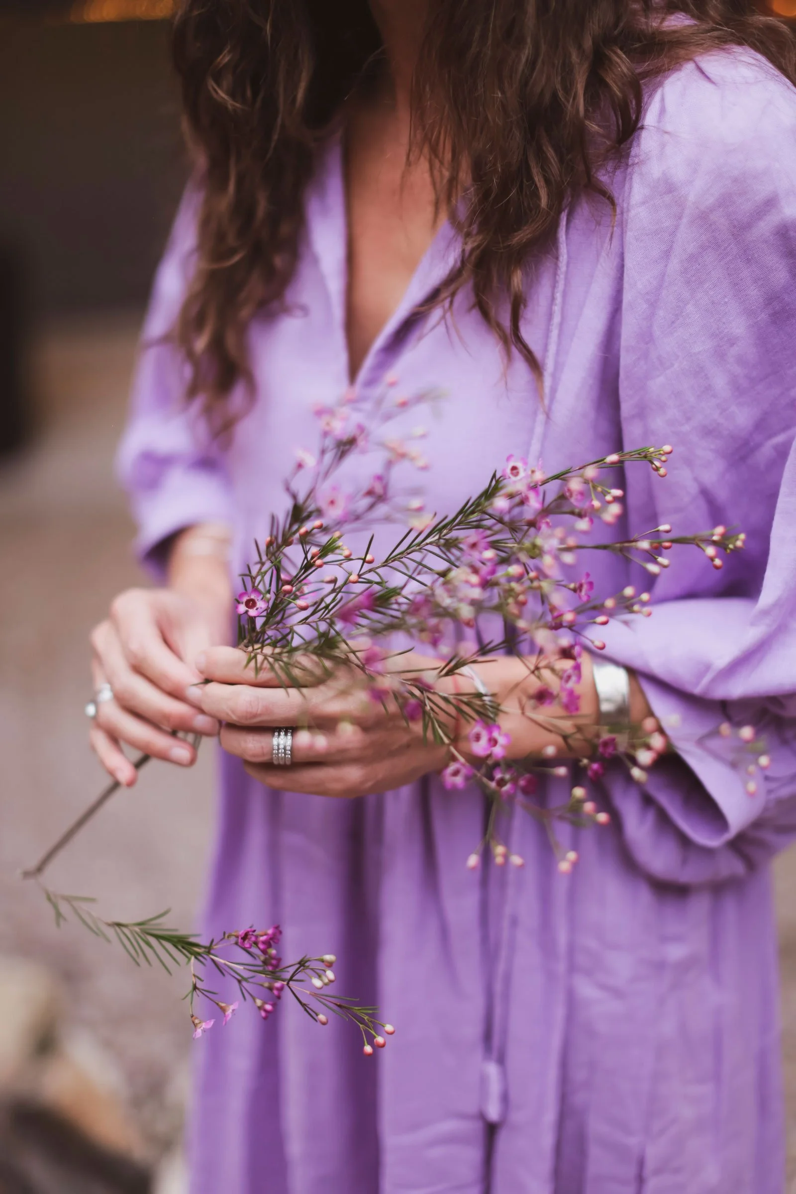 A woman in a light purple dress holding pink and purple wildflowers.