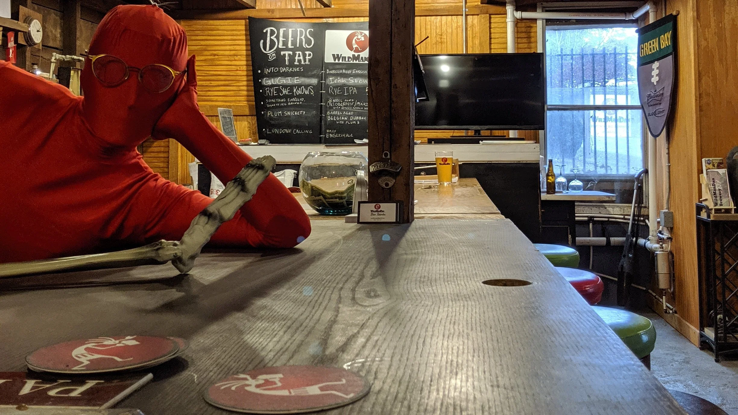 Interior of a cozy  dive bar with a quirky vibe and great beer.  A bar culture that is laid back and the retirement dream of WildManDan and Terri. A chalkboard menu lists beers on tap, and various glasses and bottles are visible near the window.