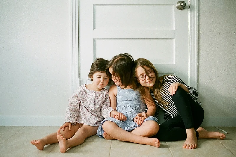  film portrait of three sisters sitting next to eachother on the floor by award winning Maternity, Baby, and Family Photographer, Mae Burke- Photographing families in and visiting Rockport, Port Aransas, Corpus Christi, Austin, Houston and Dallas/For