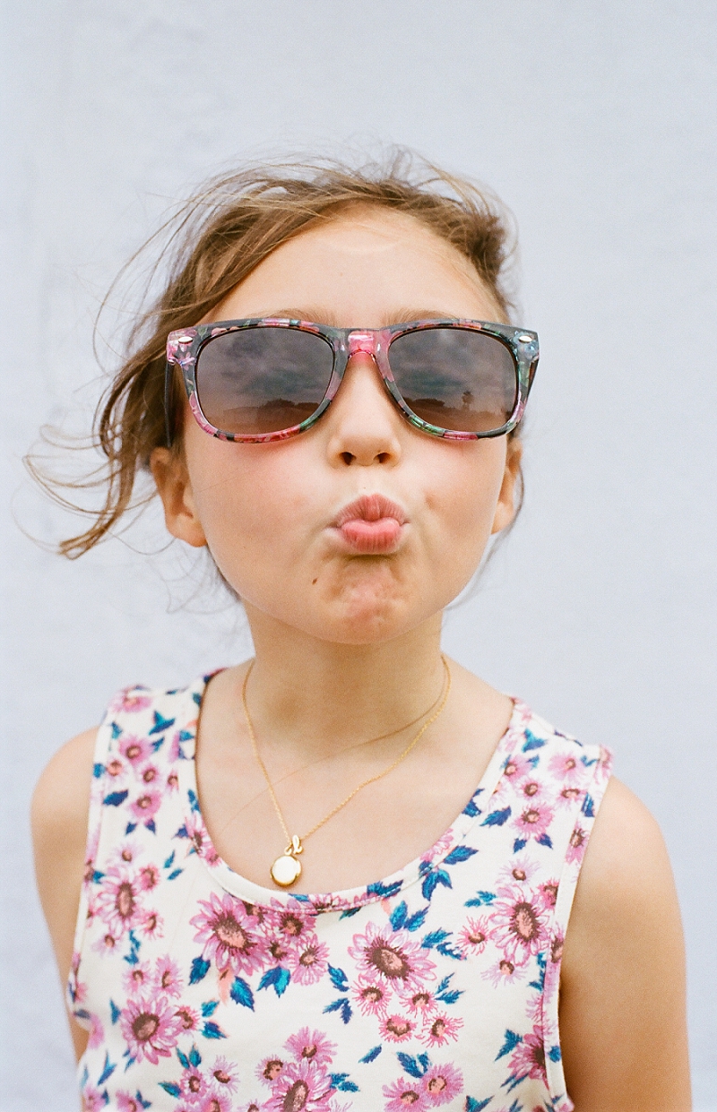  FIlm image of little girl making a fish face wearing sunglasses and a floral dress by award winning Maternity, Baby, and Family Photographer, Mae Burke- Photographing families in and visiting Rockport, Port Aransas, Corpus Christi, Austin, Houston a