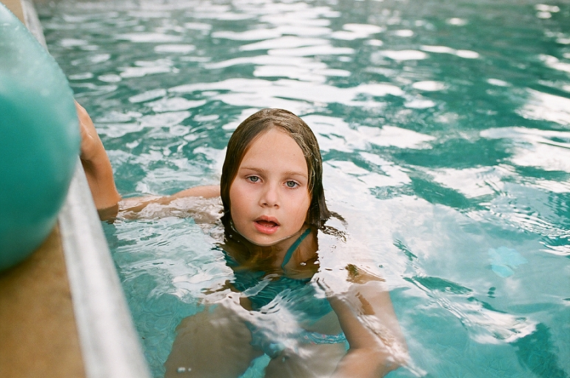  Film image of young girl hanging on the edge of a pool by award winning Maternity, Baby, and Family Photographer, Mae Burke- Photographing families in and visiting Rockport, Port Aransas, Corpus Christi, Austin, Houston and Dallas/Fort Worth, Texas.