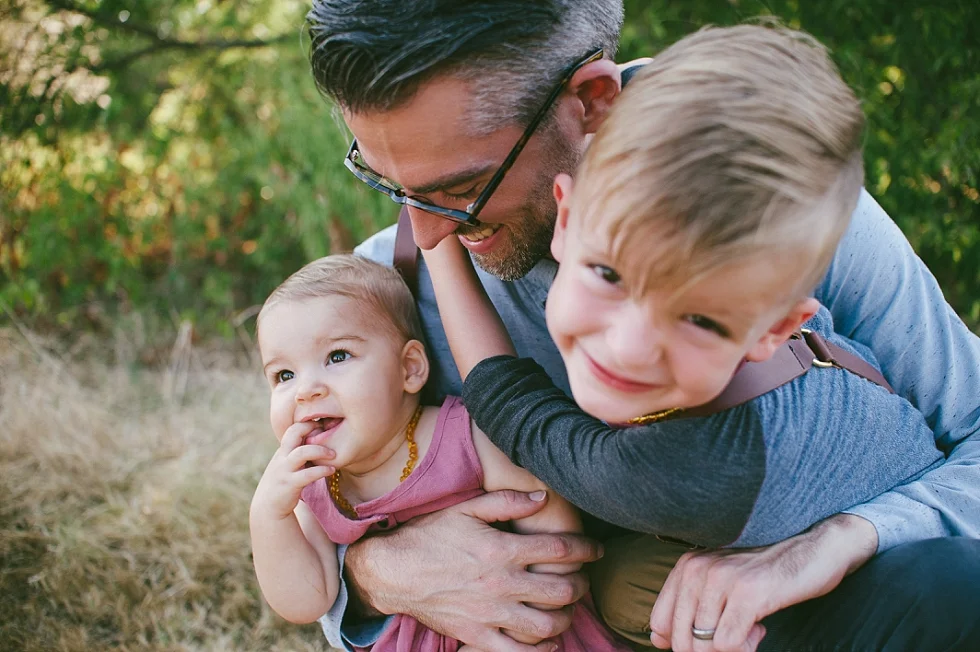  Father holding baby girl and son laughing during an on-location family session with award winning Maternity, Baby, and Family Photographer, Mae Burke- Photographing families in and visiting Rockport, Port Aransas, Corpus Christi, Austin, Houston and