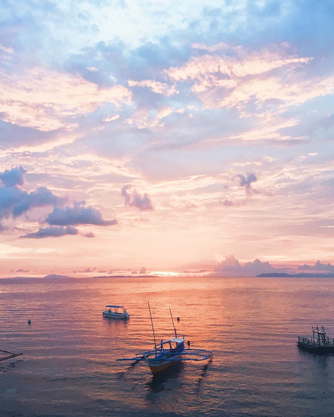 与漂浮在仍然水的紫色云彩和渔船的桃红色日落在菲律宾的水