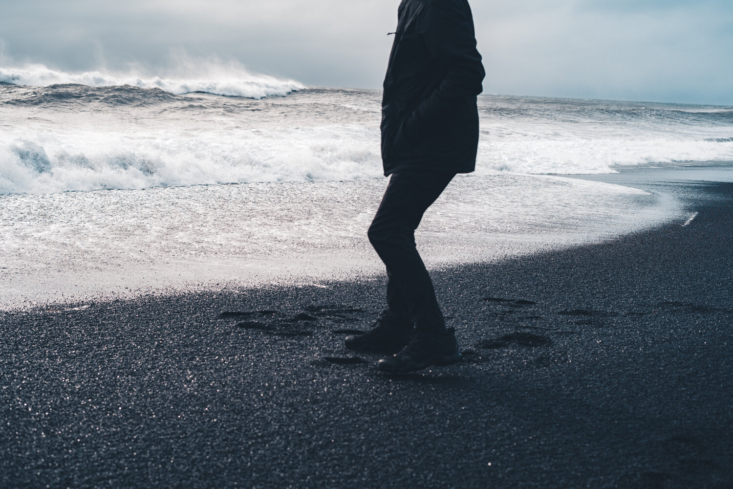 有人站在黑色的沙滩上，踏着脚步走向海边，背景是海浪