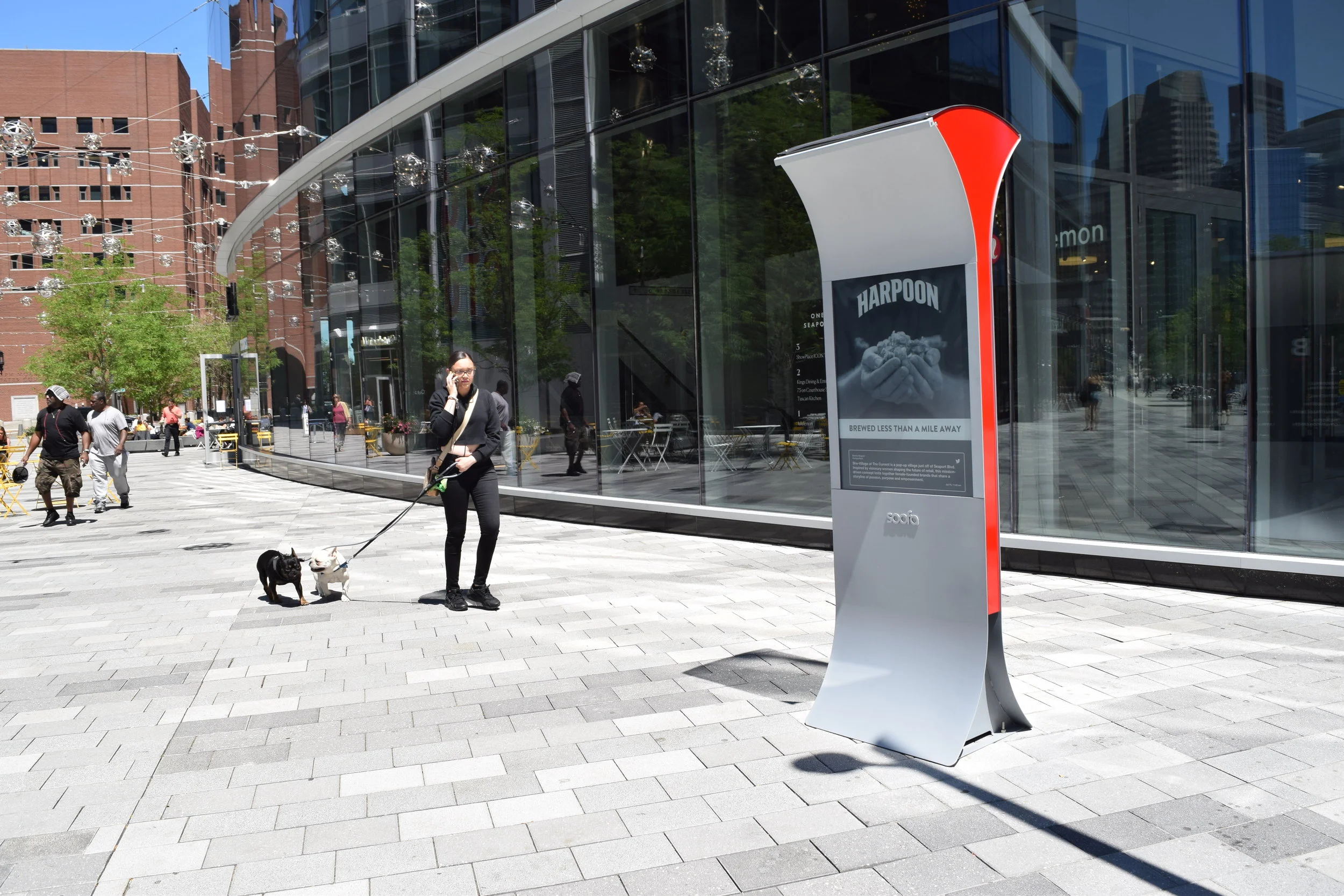 A pedestrian and dog pass by a Soofa Sign