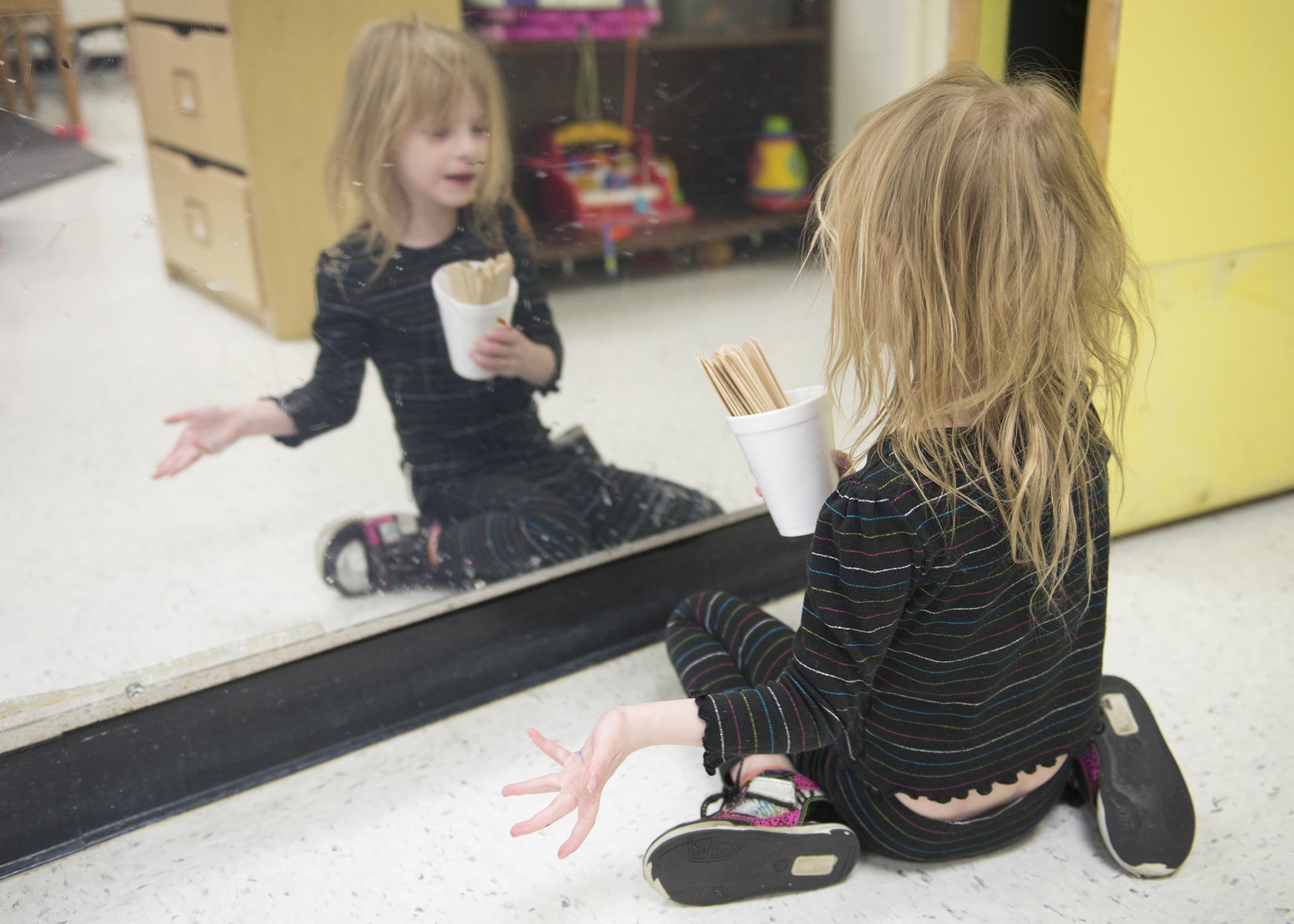 Shirley Anderson looks at herself in the mirror. At times Shirley would go over to the large mirror in the classroom and either look or interact with herself (like she is doing here) or she would bring toys in front of the mirror and would play with them there. She would seem much calmer in front of the mirror if before she seemed a little agitated.