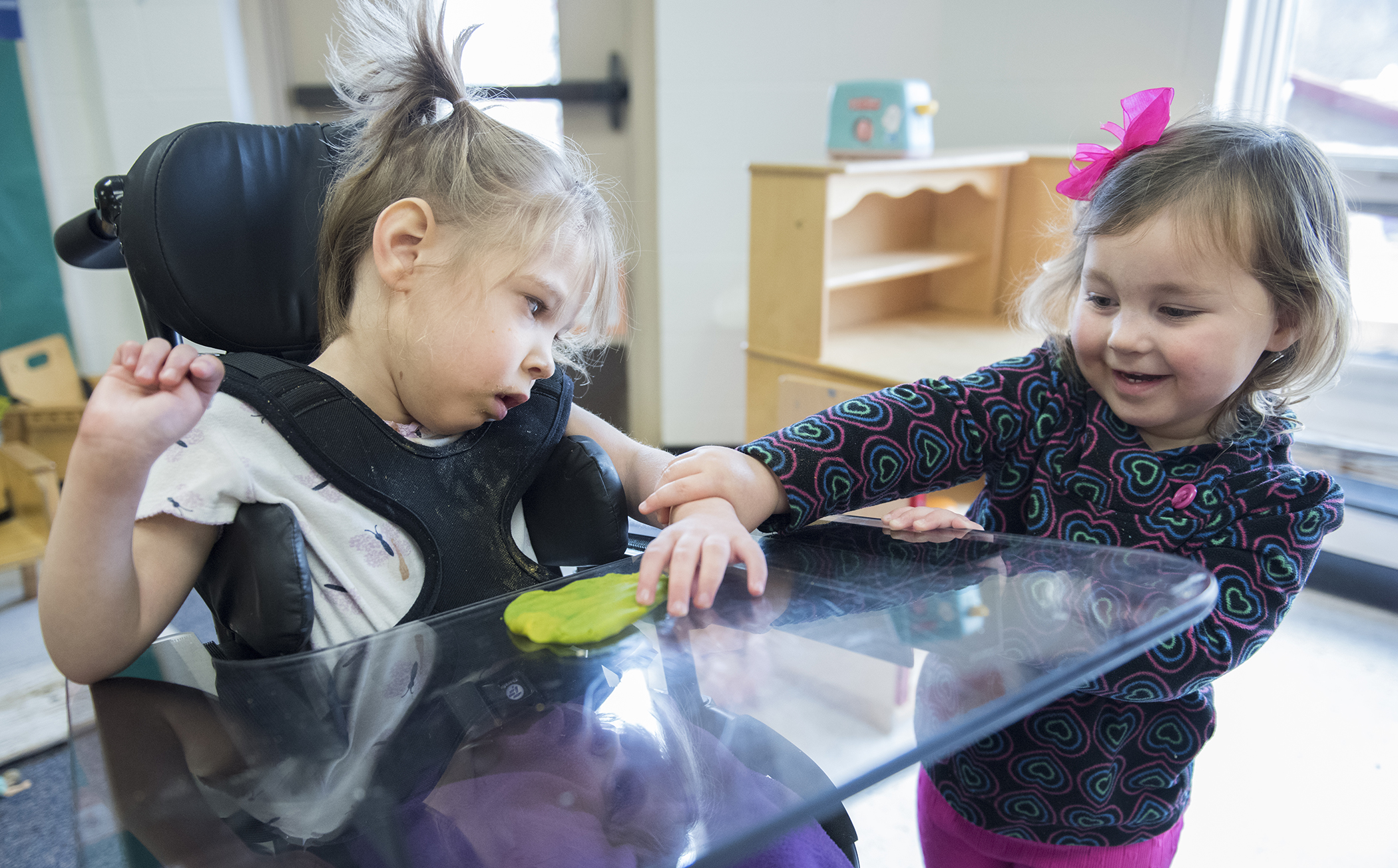 Emily Stack plays with Karman during class. Karman was given the play-dough to help her feel different textures and has also used pompoms and fuzzy balls to help with sensory skills. Because of Karman's cerebral palsy, learning to feel different textures is key. Despite Karman's difficulties with verbal communication her classmates still reach out to her and find alternative ways to communicate. Later in the day, Emily was singing the ABC's to Karman and classmate Fiona helped chime in as best as she could even though she too is non-verbal.