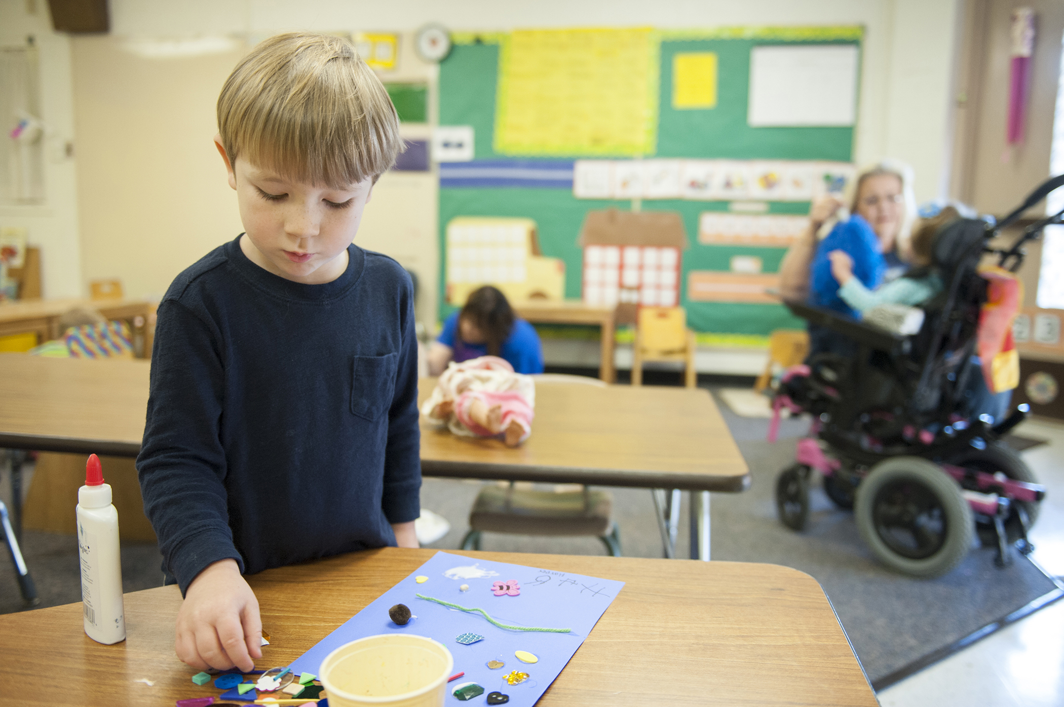 Harper puts the finishing touches on an art piece during the art session while Debbie Dixon (behind right) plays with Karman Jenkins with a pom-pom.
