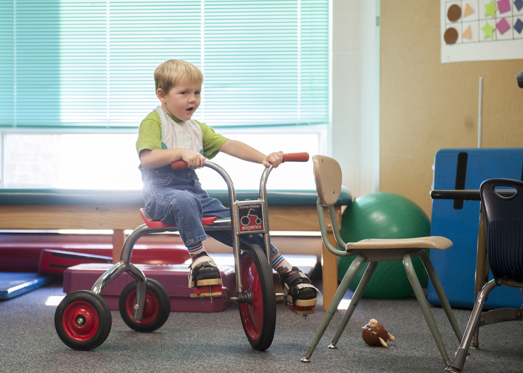 Ronnie Riley wheels around the Sensory Room on his tricycle. Ronnie went with Alania Harper, the PTA at the Beacon School, to do individual physical training, and is one of the 7-8 students Ms. Harper sees each day. Ronnie is wearing the wooden blocks on the bottom of his feet to serve as an extra layer of balance.
