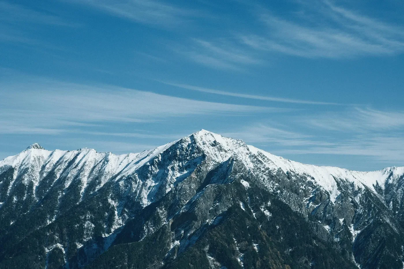 Snow-capped mountain peak beneath streaked blue sky
