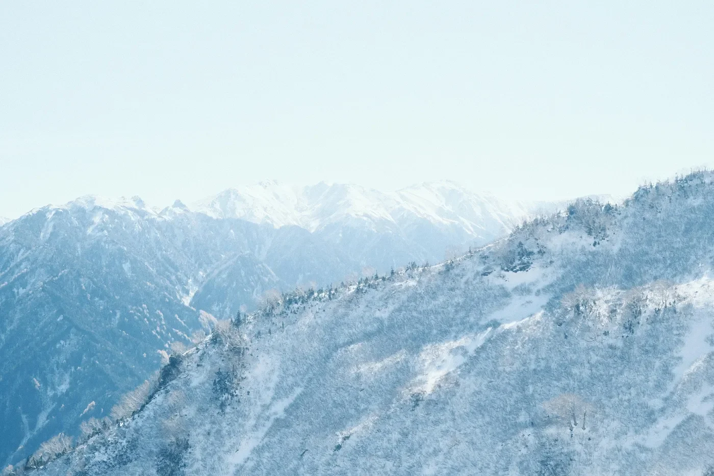 Snow-covered mountain ridge fading into a pale winter horizon