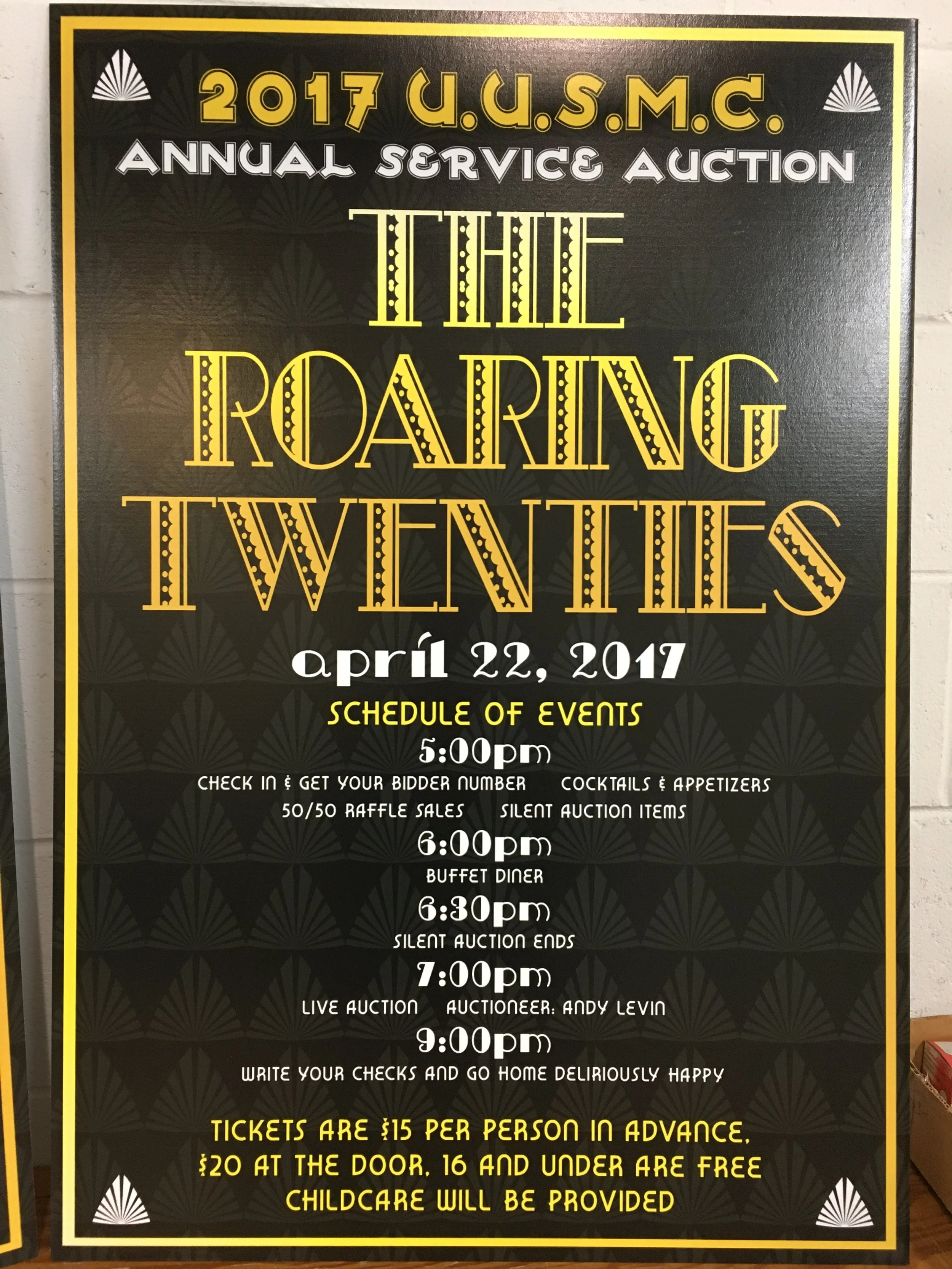 Black poster with yellow and white text detailing the schedule of events for the 2017 U.S.M.C. Annual Service Auction, titled 'The Roaring Twenties,' held on April 22, 2017. The schedule includes check-in, raffle, buffet dinner, silent auction, live 