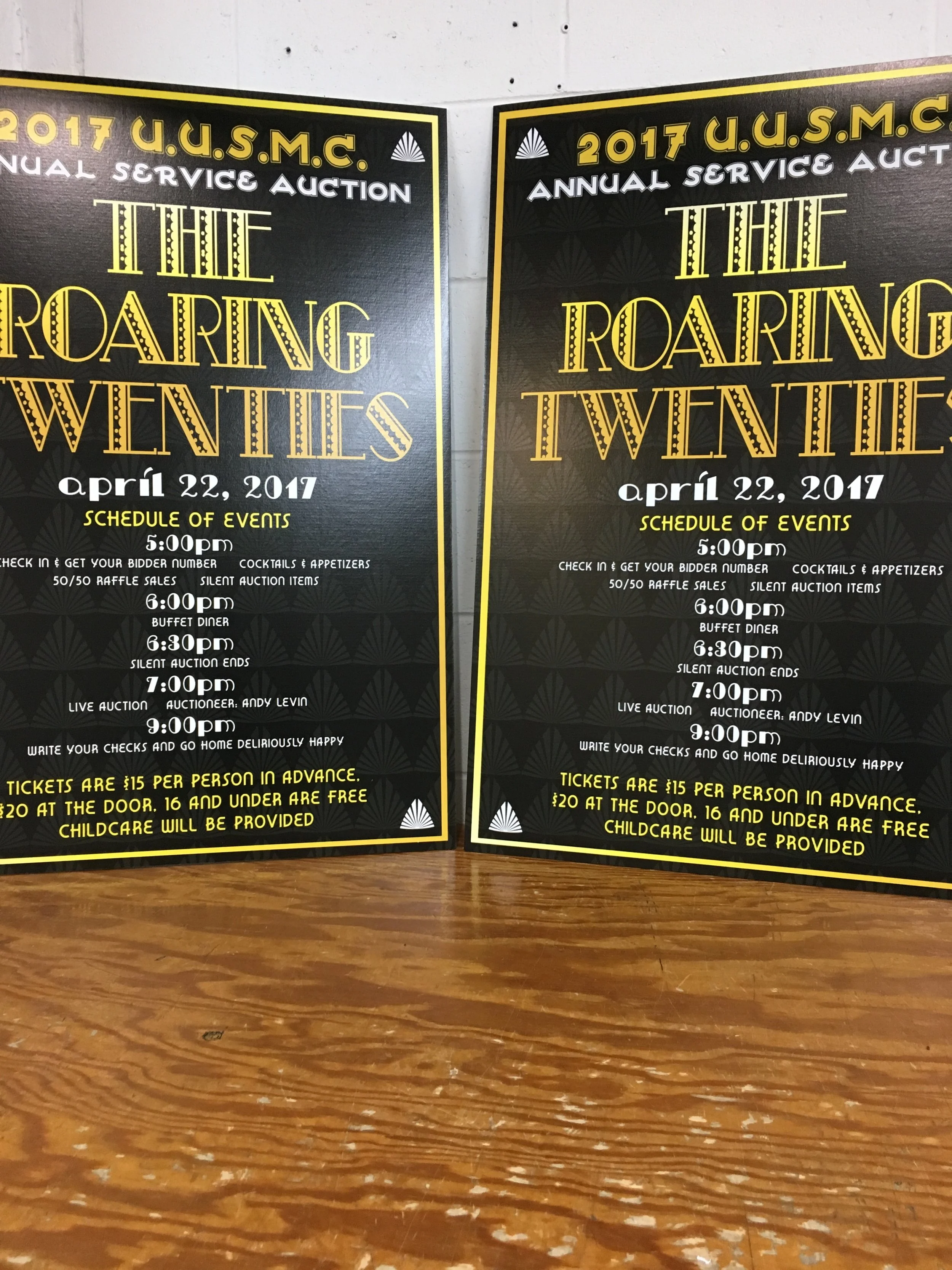 Two black event posters with yellow and white text for the 2017 U.S.M.C. Annual Service Auction called 'The Roaring Twenties,' held on April 22, 2017, listing the schedule of events from 5:00 PM to 9:00 PM, ticket prices, and childcare information.