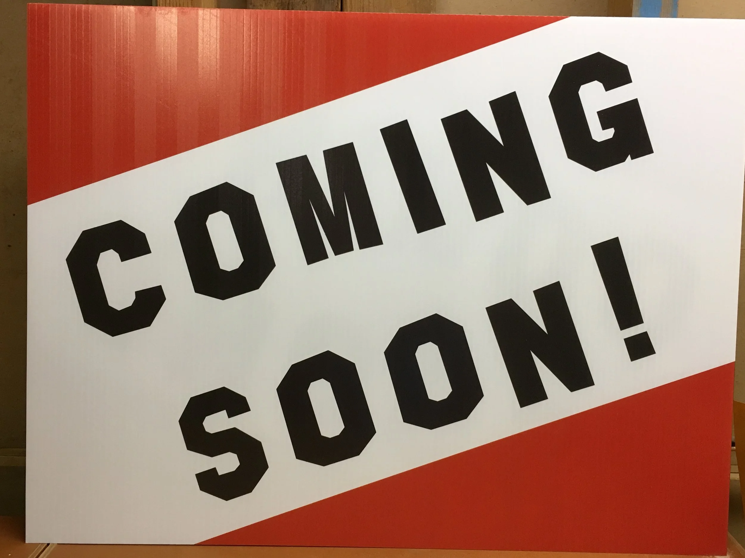Sign with red and white background reading 'COMING SOON!' in bold black letters.