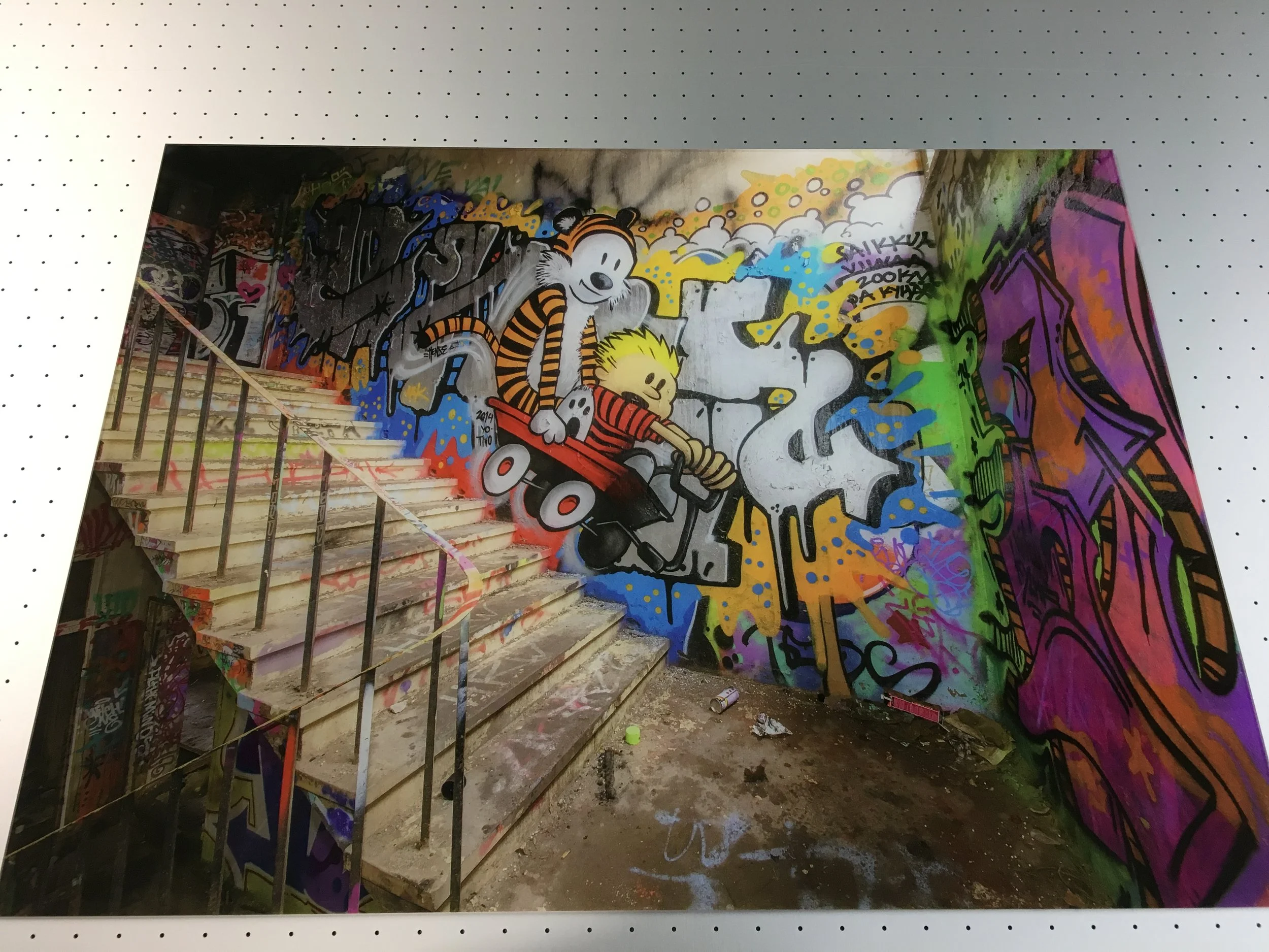 Colorful graffiti art on a wall depicting Calvin and Hobbes riding a skateboard, with vibrant spray-painted background and an unfinished staircase in the foreground.
